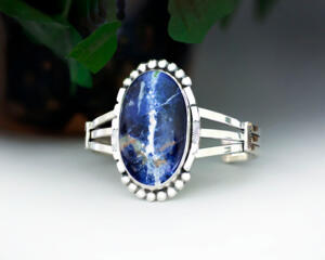 front view large blue with white veining oval sodalite jasper stone bezel set accented with beads and stamped cutout wire on a 3 wire cuff